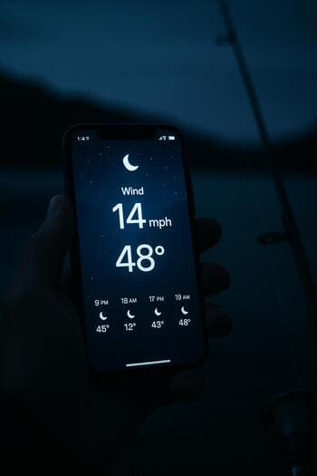 Экран смартфона с прогнозом погоды перед ночной рыбалкой